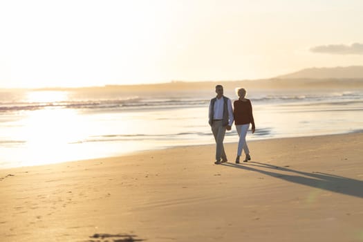 Happy retired couple enjoying a romantic walk on the beach at sunset