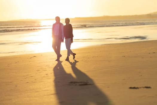 Elderly couple holding hands and walking along the shore during a golden sunset