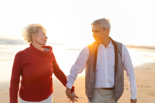 Senior couple enjoying a romantic walk on the beach at sunset, holding hands and looking at each other