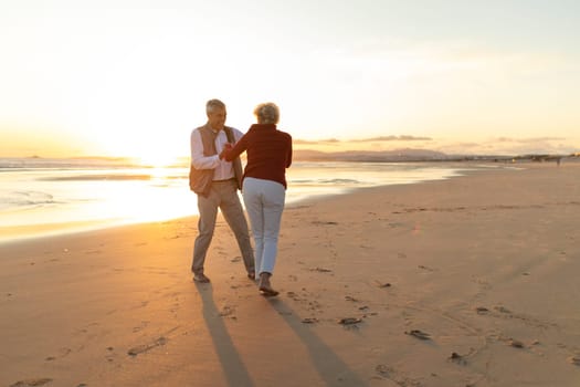Elderly couple enjoying a romantic moment, dancing on the beach at sunset