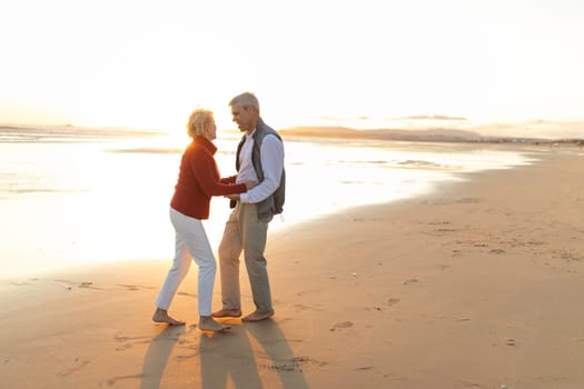 Elderly couple enjoying a romantic moment, dancing together on the beach during a beautiful sunset
