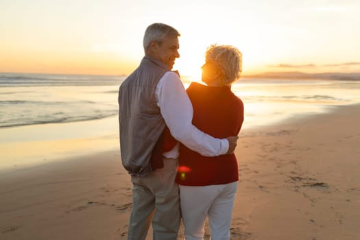 Elderly couple enjoying a romantic moment on the beach at sunset, embracing and looking at each other with love and affection
