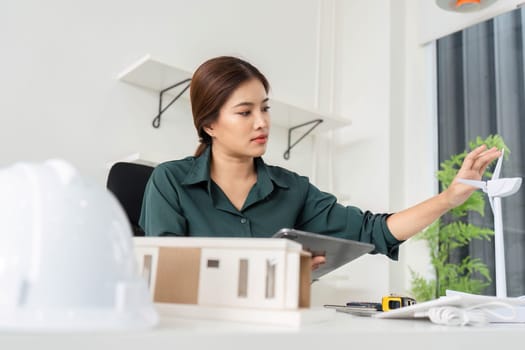 A woman architect inspects a sustainable model while using a tablet to enhance project accuracy in a bright office.