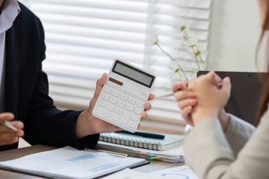 A businessman shows a calculator to a client during a financial consultation, emphasizing important data analysis in a modern office.