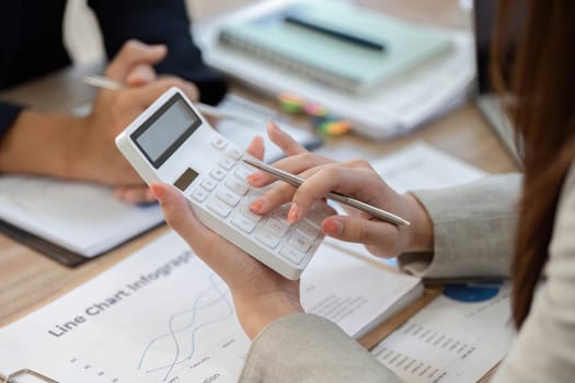 A professional woman uses a calculator while analyzing financial data, emphasizing precision and strategy in a modern office.