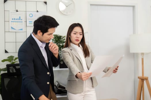 Two business professionals engage in a strategic discussion, reviewing project documents and collaborating in a contemporary office environment.
