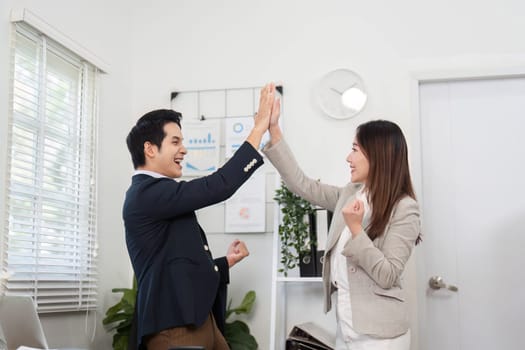 Two business professionals joyfully high-fiving in a bright office, symbolizing teamwork and success in their careers.