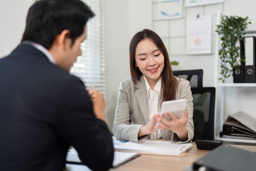 A client smiles while reviewing financial information on a smartphone with a financial advisor in a modern office setting.