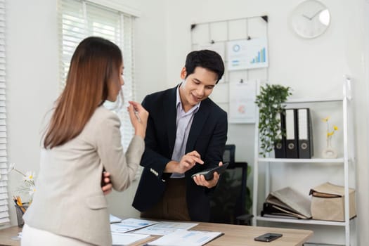 A businesswoman and businessman review project data on a tablet, emphasizing teamwork and technology in a modern office setting.