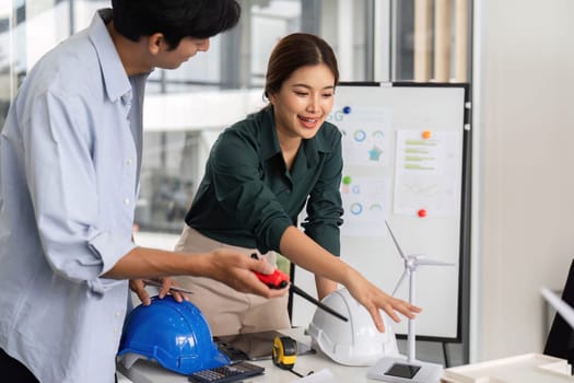 Two engineers discussing and measuring for a renewable energy project, focusing on wind energy solutions in a modern office.