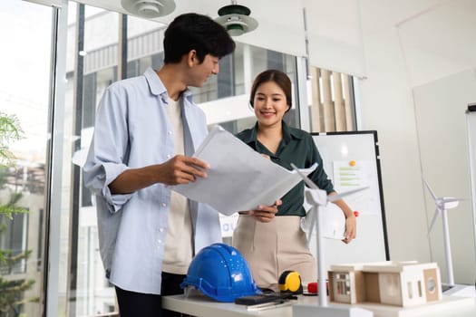 Two engineers reviewing blueprints and celebrating teamwork in a contemporary workspace. Concept of innovation and collaboration.