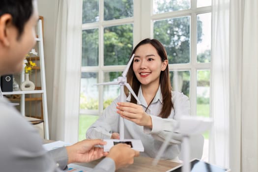 A business professional hands a wind turbine model to a colleague during an ESG-focused collaboration on sustainability strategies.