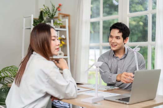 Business professionals collaborate on ESG-focused renewable energy projects, discussing ideas with wind turbine models in an inviting workspace.