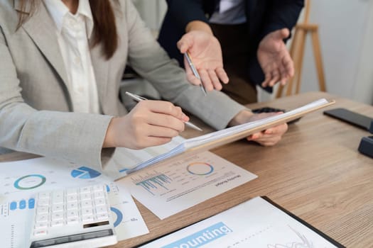 A business professional analyzing financial reports and charts while discussing strategies with a colleague in an office.