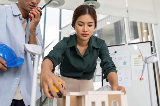 A female architect measures a model during a planning session, focusing on details for a sustainable building project.