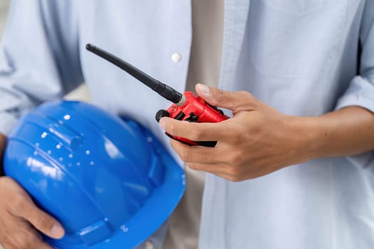 An engineer holds a blue safety helmet and a walkie-talkie, emphasizing safety and communication in construction projects.