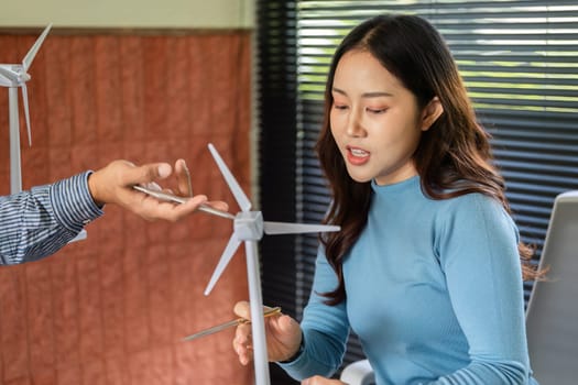 A woman engages with a male colleague about a wind turbine model, emphasizing sustainability in engineering.