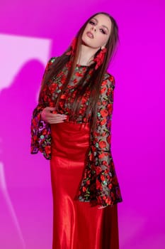 A striking model showcases a stunning red dress with floral detailing against a vibrant pink backdrop.