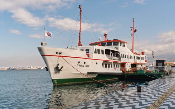 Izmir, Turkey - April 6, 2025: White and red ferry ZUBEYDE HANIM docked at Kordon pier. City skyline in background