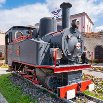 Izmir, Turkey - April 6, 2025: Historic TCDD steam locomotive No. 97, Turkish State Railways building, Konak district. Vintage black engine with red trim, on display among flowers