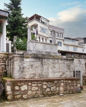 Historic stone tomb with decorative carvings and modern buildings in the background, at the courtyard of Cinili Mosque in Uskudar, Istanbul, Turkey