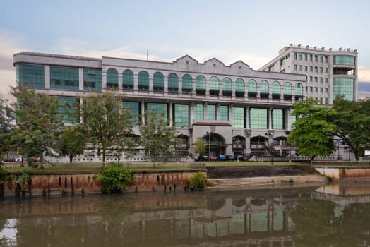 Mall Gadong stands prominently by the river in Bandar Seri Begawan, Brunei, featuring modern architecture and lush palm trees. Visitors enjoy shopping and leisure activities in this bustling complex