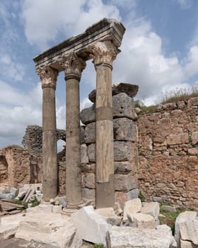 Historic ruins featuring three ancient columns with ornate capitals and stone walls at Ephesus, Selcuk, Turkey. Archaeological site under cloudy sky