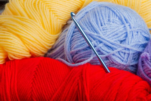 A blue crochet hook is sitting on top of a pile of yarn. The yarn is in various colors, including red, yellow, and blue. Concept of creativity and craftsmanship