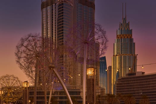 UAE, Dubai, 11 December 2024: The famous Burj Khalifa skyscraper through the art object metal dandelions at dusk, Dubai's sights during the incredible sunset sky, skyscrapers illuminated. High quality photo