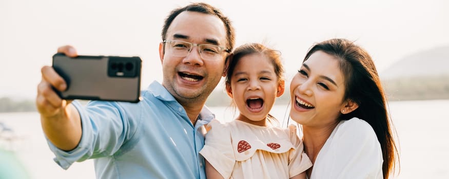 Asian family taking selfie picture with smartphone outdoor nature park, Happy smile father mother and child daughter taking photo with mobile phone together, Tourist lifestyle people leisure activity