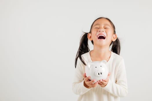 Asian little kid girl holding piggy bank and looking at camera at studio isolated on white background, Happy kindergarten child lifestyle smiling with is white piggybank, Thai personal money savings
