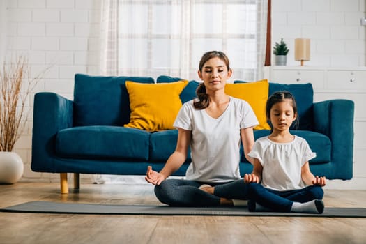 In a heartwarming family yoga session a mother and her daughter practice yoga in lotus position promoting mindfulness and meditation with smiles reflecting their joy and togetherness.