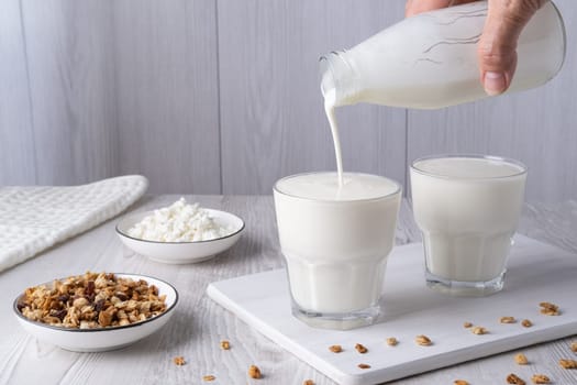 Pouring homemade kefir, buttermilk or yogurt with probiotics. Yogurt flowing from glass bottle on light background. Probiotic cold fermented dairy drink. Trendy food and drink. Copy space.
