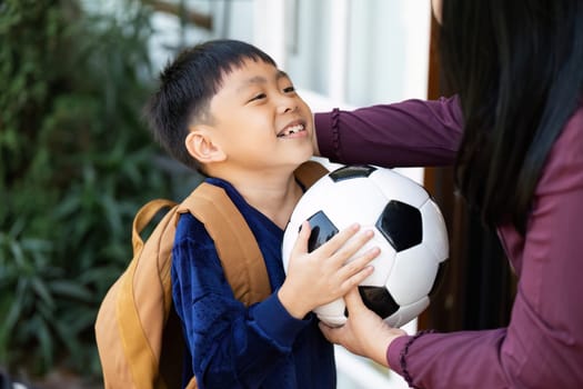 A cheerful boy holds a soccer ball and sports a backpack, ready to embark on a new school year filled with excitement and sports activities.