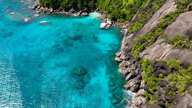 A rocky coastline with striking turquoise water and dense green vegetation on the slopes. Seychelles, Mahe.