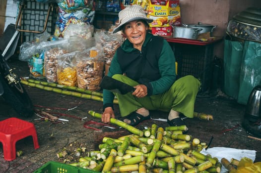A Vietnamese woman slices sugar cane with a machete at a local market. Nha Trang, Vietnam - December 16, 2024