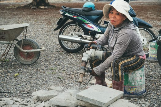 An adult Vietnamese woman works at a construction site with an electric jackhammer. Nha Trang, Vietnam - December 16, 2024