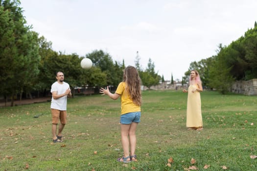 Happy family enjoying leisure time, playing volleyball together in green park