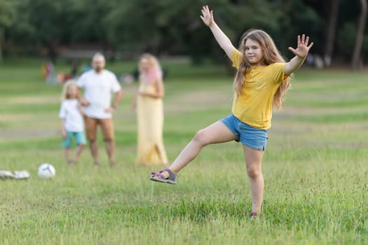 Young girl dancing in a park while her family watches in the background, enjoying a leisurely summer day together