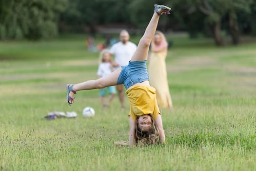 Girl doing a cartwheel in a park while her family watches in the background, enjoying a sunny day outdoors