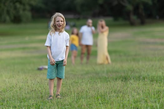 Happy blond boy standing in a grassy field, enjoying leisure time with his family in a park setting