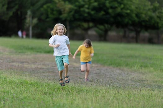Two joyful kids running on grass in a park, enjoying summer holidays