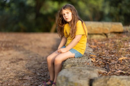 Girl enjoying a peaceful moment in a park, sitting on a rock amidst dry leaves