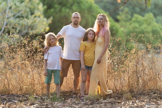 Family with two children posing together outdoors in tall grass at golden hour