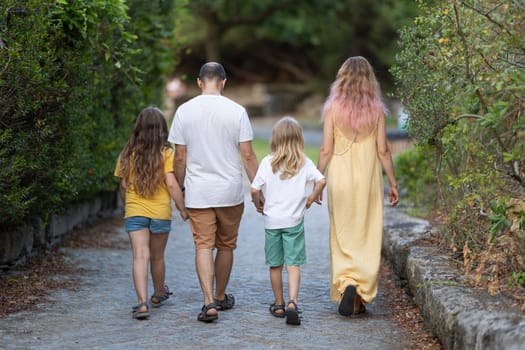 Family of four walking away on a path in a park, holding hands