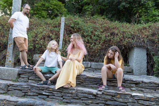 Family with two children enjoying summer vacation in a park, sitting on stone steps