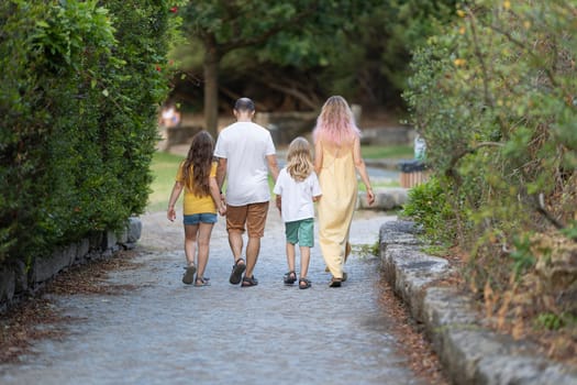 Family of four walking away on a path in a park, holding hands