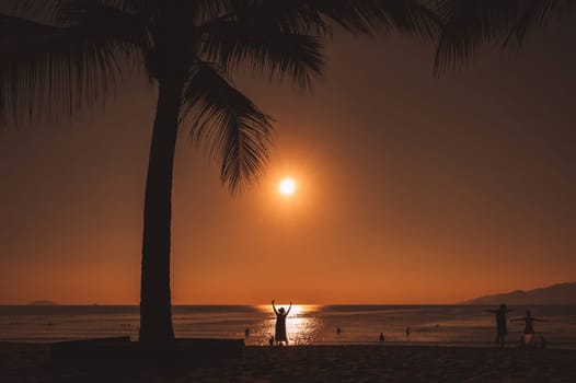 silhouette of a woman doing exercises on the beach with a palm tree by the sea in the morning on vacation