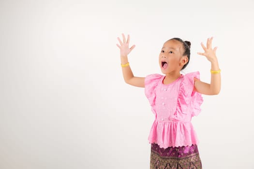 Portrait Thailand kid girl smiling traditional Thai dress costume raises fists in celebration of her success, studio isolated white background, kindergarten child saying yes with excitement winning