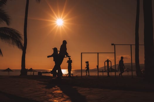 silhouettes of elderly Vietnamese people on horizontal bars at a sports ground by sea doing exercises in morning at sunrise